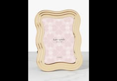 a pink and gold frame with the words kate spade on it, in front of a white background