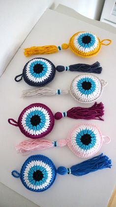 several crocheted eyeball ornaments are arranged on a white surface with blue and yellow tassels