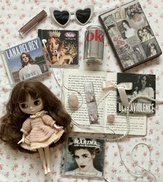 an assortment of dolls, magazines and other items are laid out on a bed sheet