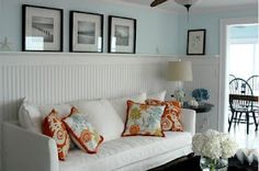 a living room filled with white furniture and pictures on the wall above it's windows