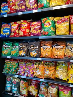 many bags of chips are on display in a store shelf with other snacks behind them