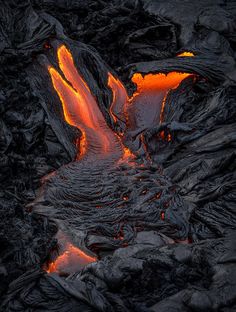 lava flowing down the side of a mountain with bright orange light coming from it's mouth