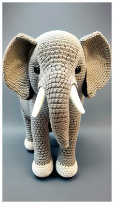 an elephant made out of knitted yarn with tusks and ears, standing on a gray background