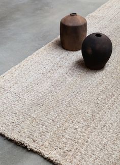 two black vases sitting on top of a white rug next to a brown vase