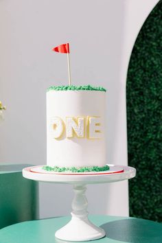 a white cake with green frosting and a red flag on top that says one