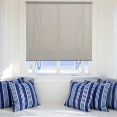 a window with blinds and pillows in front of it, next to a white bench