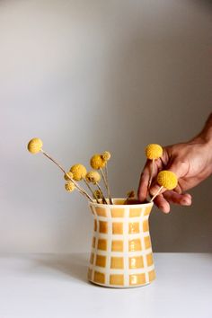 a person is arranging yellow flowers in a white and yellow vase on a table,