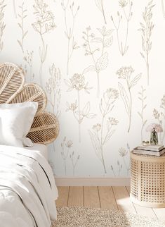 a white bed sitting next to a wall with flowers on it and a wicker side table