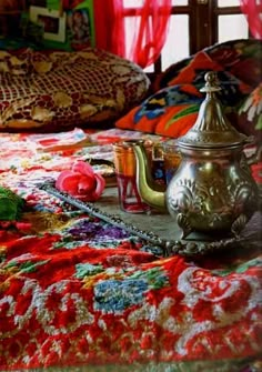 a tea pot sitting on top of a bed covered in colorful blankets and rugs