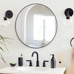 a bathroom sink under a round mirror next to a potted plant and candle holder