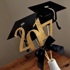 a black and gold graduation hat on top of a white vase with sticks in it