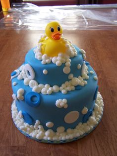 a blue cake with white icing and a rubber ducky on top, sitting on a wooden table