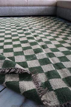 a green and white checkered rug sitting on top of a floor next to a couch