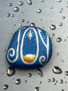 a painted rock sitting on top of a metal surface covered in water drops and snow