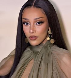 a woman with long black hair wearing large earrings and a sheer green dress is looking at the camera