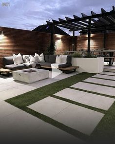 an outdoor living area with grass, couches and lights on the side of the building