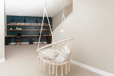 a hammock chair hanging from the ceiling in a room with shelves and desks