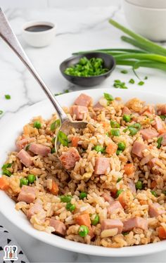 a white bowl filled with rice and ham on top of a table next to green onions