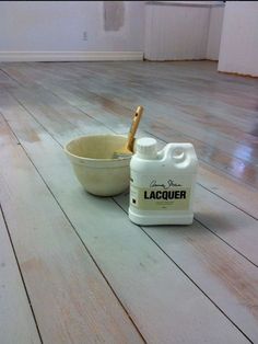 a white container with a wooden spoon in it on the floor next to a gallon of lacquer