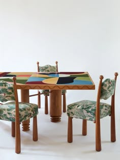 a wooden table with chairs around it in front of a white wall and an abstract painting on the table