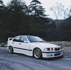 a white car parked on the side of a road next to some rocks and trees