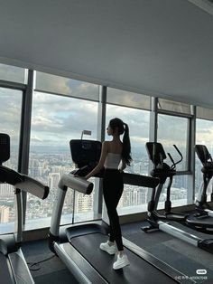 a woman is standing on a treadmill in front of a window overlooking the city