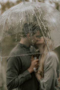 a man and woman kissing under an umbrella in the rain while holding each other's hands