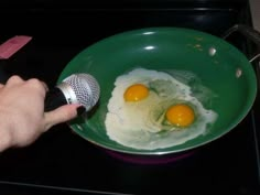 two eggs being fried in a green bowl with a microphone on the stove top next to it