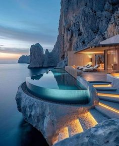 an outdoor swimming pool with steps leading to it and the ocean in the background at dusk