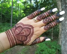 a woman's hand with henna tattoos on it and trees in the background