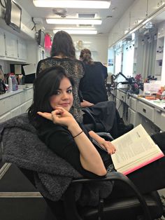 a woman sitting in a chair with a book on her lap and looking at the camera