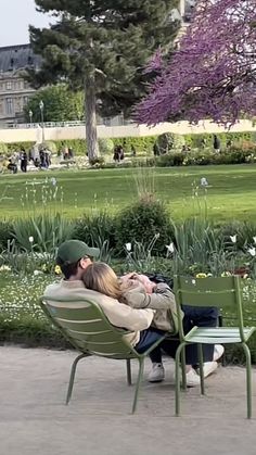 a man and woman sitting on top of a green bench in front of a park