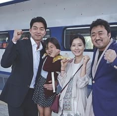 three people standing next to each other in front of a blue and white passenger train