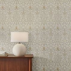 a white lamp sitting on top of a wooden dresser next to a wallpapered wall