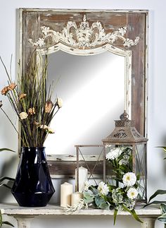 a mirror sitting on top of a white mantle next to flowers and a vase filled with plants