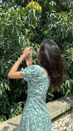 a woman in a green dress is taking a picture with her cell phone while standing next to some trees