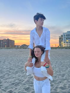 two people standing on top of each other at the beach with buildings in the background