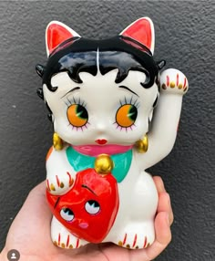 a white cat figurine with orange eyes holding a red heart in it's paws