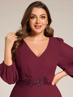 a woman wearing a burgundy dress with long sleeves and an embellishment on the waist