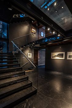 an empty room with stairs and pictures on the wall in front of glass windows, at night