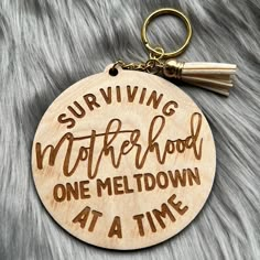 a wooden keychain that says surviving motherhood one meltdown at a time