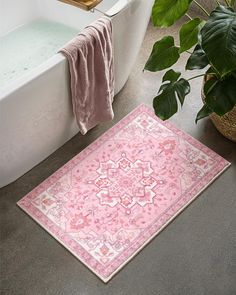 a bath tub sitting next to a pink rug on top of a bathroom floor near a plant