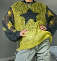 a woman wearing a yellow and black sweater with stars on the top, standing in front of a bed