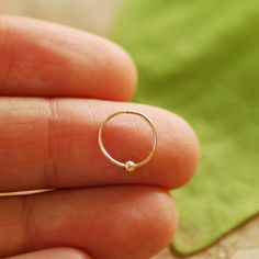 a hand holding a tiny gold ring with a small bead on the inside of it