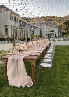 a long table is set up with pink flowers and candles for a wedding reception in the grass