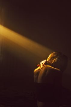 a woman standing in the dark with her back turned to the camera and light coming from behind her