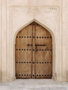 an arched wooden door with metal bars on the outside and inside, in front of a white stucco wall