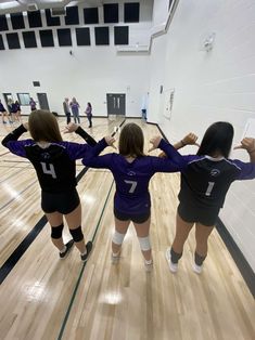 three girls in volleyball uniforms standing on a court with their arms around each other's shoulders