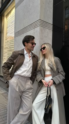 a man and woman standing next to each other in front of a building with their arms around each other