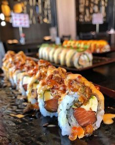 several sushi rolls are lined up on a black counter with other food items in the background